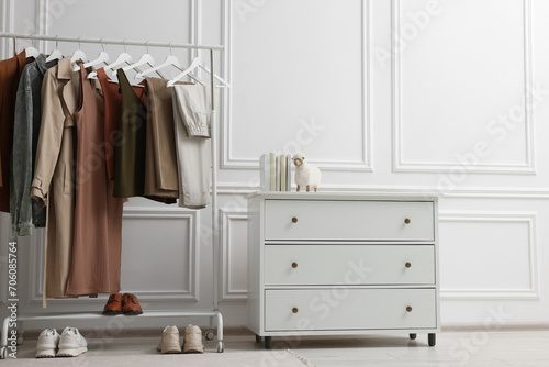 Rack with different stylish women`s clothes, shoes and dresser near white wall in room © New Africa