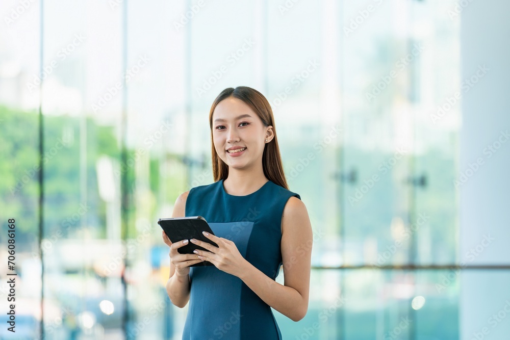 Young Asian Woman Smiles Happily While Using Digital Tablet to Manage Her Tasks Remotely While Out Of Office