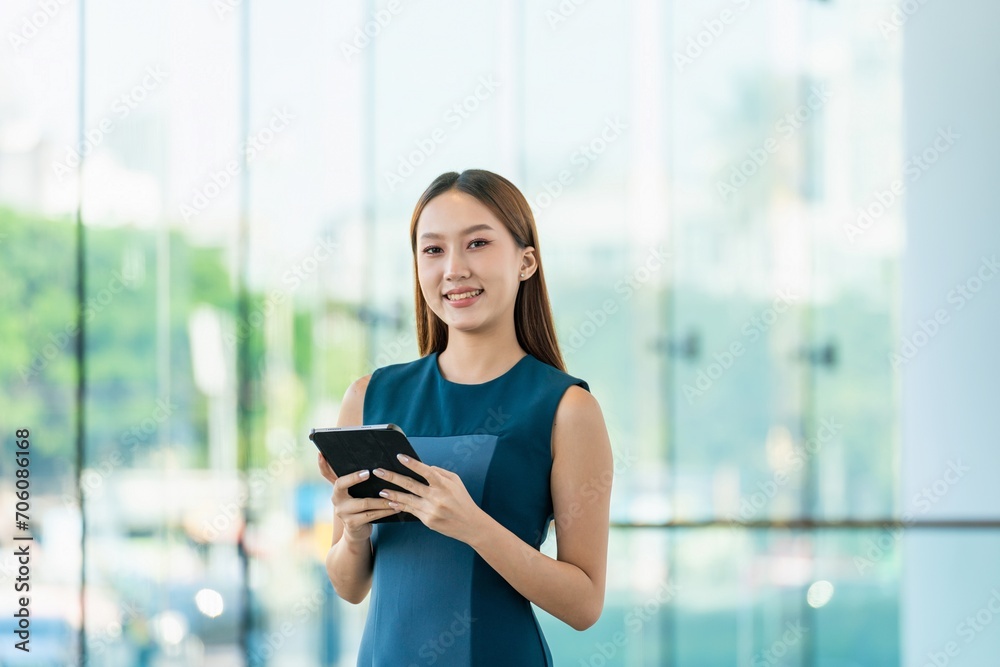 Young Asian Woman Smiles Happily While Using Digital Tablet to Manage Her Tasks Remotely While Out Of Office Young Asian Woman Smiles Happily While Using Digital Tablet to Manage Her Tasks Remotely While Out Of Office
