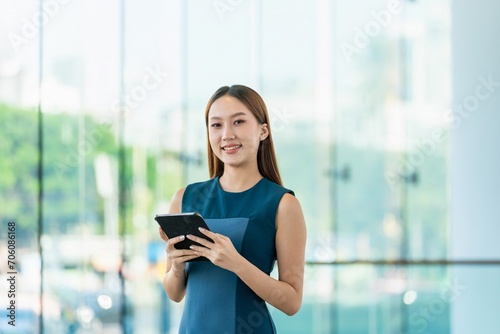 Young Asian Woman Smiles Happily While Using Digital Tablet to Manage Her Tasks Remotely While Out Of Office © asean studio