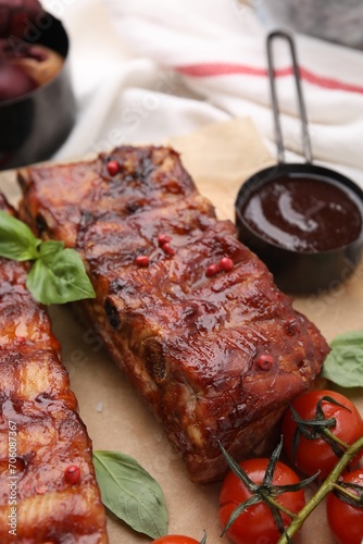 Tasty roasted pork ribs served with sauce, basil and tomatoes on table, closeup