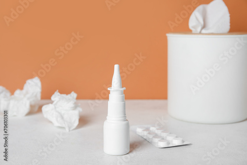 Nasal drops with pills and tissue box on table near orange wall  closeup. Allergy concept