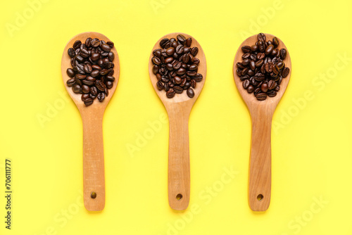 Wooden spoons with coffee beans on yellow background