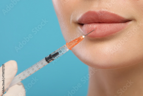 Doctor giving lips injection to young woman on light blue background  closeup. Cosmetic surgery