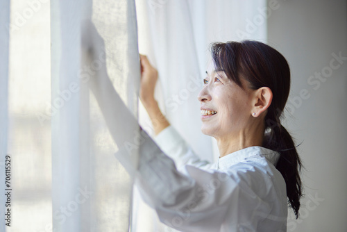 リビングのカーテンを開ける日本人のシニア女性