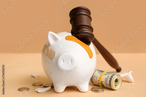 Broken patched piggy bank with judge gavel and money on orange background. Bankruptcy concept
