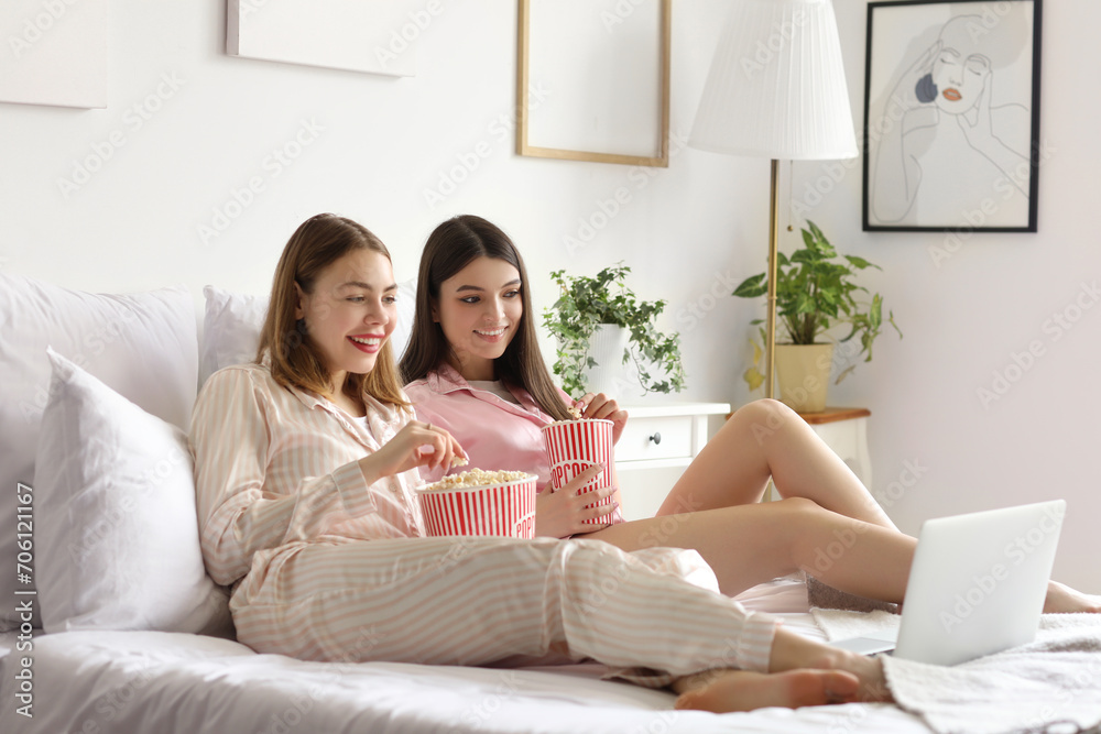 Female friends with popcorn watching movie in bedroom Female friends with popcorn watching movie in bedroom