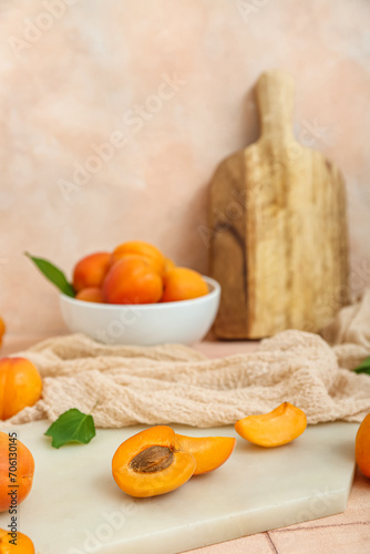 Board with bowl of fresh apricots on pink tile table