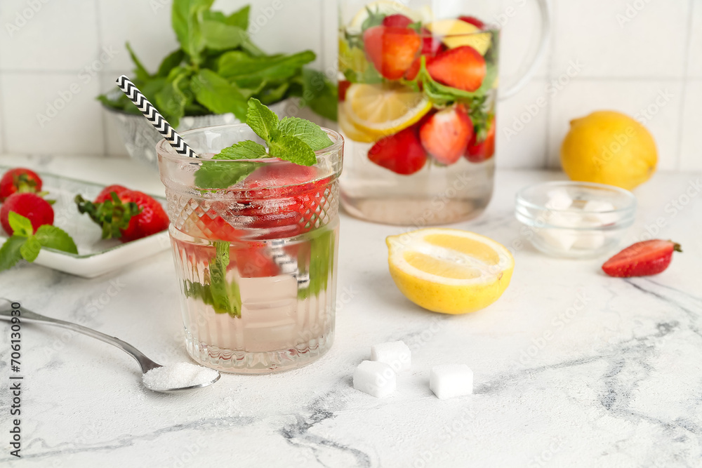 Glass and jug of fresh lemonade with strawberry on white table Glass and jug of fresh lemonade with strawberry on white table