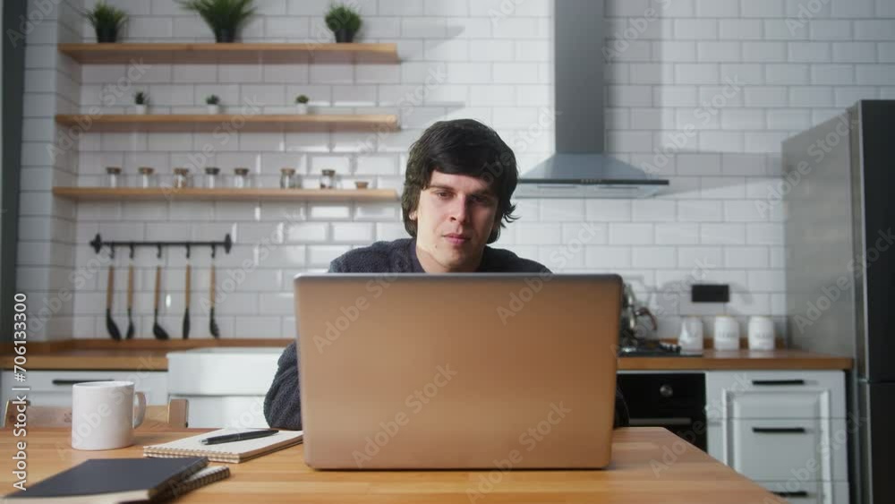 Smiling young man working at home in the kitchen working with his laptop, doing research. Busy freelancer working on modern tech notebook device Smiling young man working at home in the kitchen working with his laptop, doing research. Busy freelancer working on modern tech notebook device