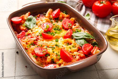 Baking dish of pasta with tomato sauce and cheese on white tile background