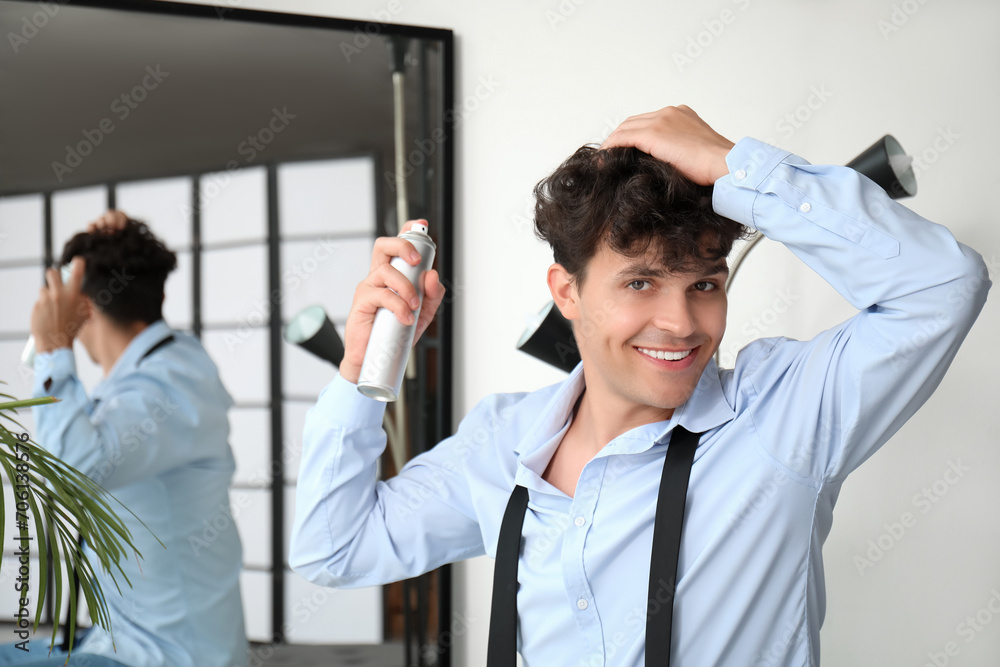 Fototapeta premium Handsome young man applying hair spray on his curly hair near mirror