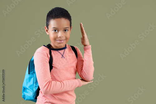 Little African-American schoolboy with raised hand on green background