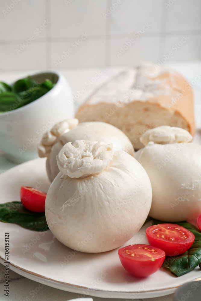Plate of tasty Burrata cheese with basil and tomatoes on white tile background Plate of tasty Burrata cheese with basil and tomatoes on white tile background