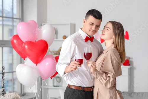 Beautiful young couple with heart-shaped balloons and glasses of wine celebrating Valentine's Day at home © Pixel-Shot