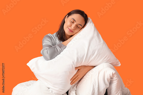Pretty young woman with blanket and pillow on orange background