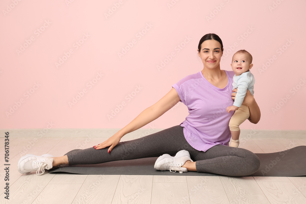 Beautiful young sporty woman with her little baby stretching near pink wall Beautiful young sporty woman with her little baby stretching near pink wall