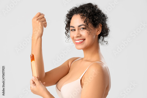 Beautiful African-American woman using sugaring paste for hair removal on white background