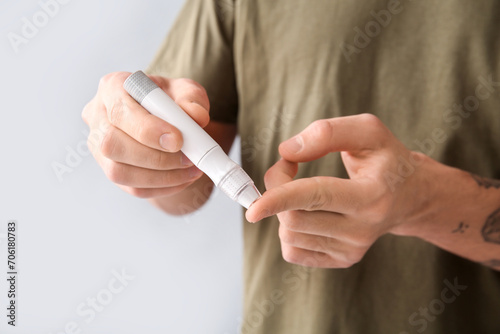 Diabetic young man using lancet pen on light background  closeup