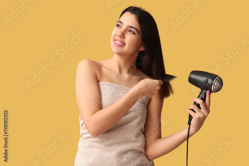 Beautiful young happy woman with towel, hair dryer and comb on yellow background
