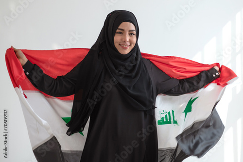 Happy Muslim woman wears black Hijab Muslim traditional clothes holding Irag flag, sunlight and shade on white wall, Muslim woman rights concept photo