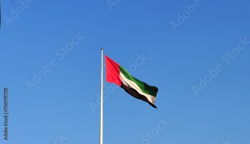 United Arab Emirates (UAE) country official national fabric or cloth flag on a flagpole flying isolated in the air by the wind on a blue sky background with copy space. Arab National Day concept.