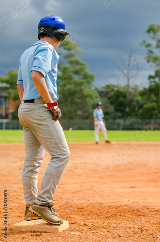 Baseball game, runner on the third base is watching the pitcher and getting ready to run to home plate and score