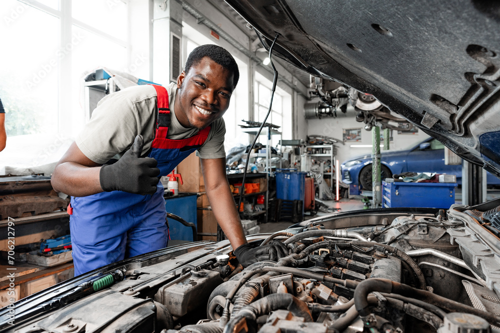Fototapeta premium Young African auto mechanic checking car engine under the hood in auto service