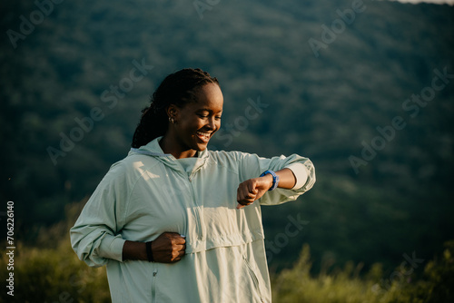 African American woman jogging gracefully in a scenic outdoor setting, checking her smartwatch for fitness progress