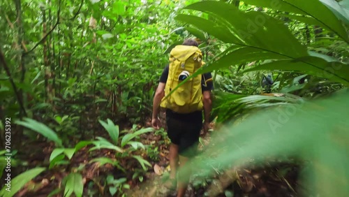 backpackers walking in deep forest jungle trekking path exploring Central America rain forest yellow bright backpack in green vegetation photo