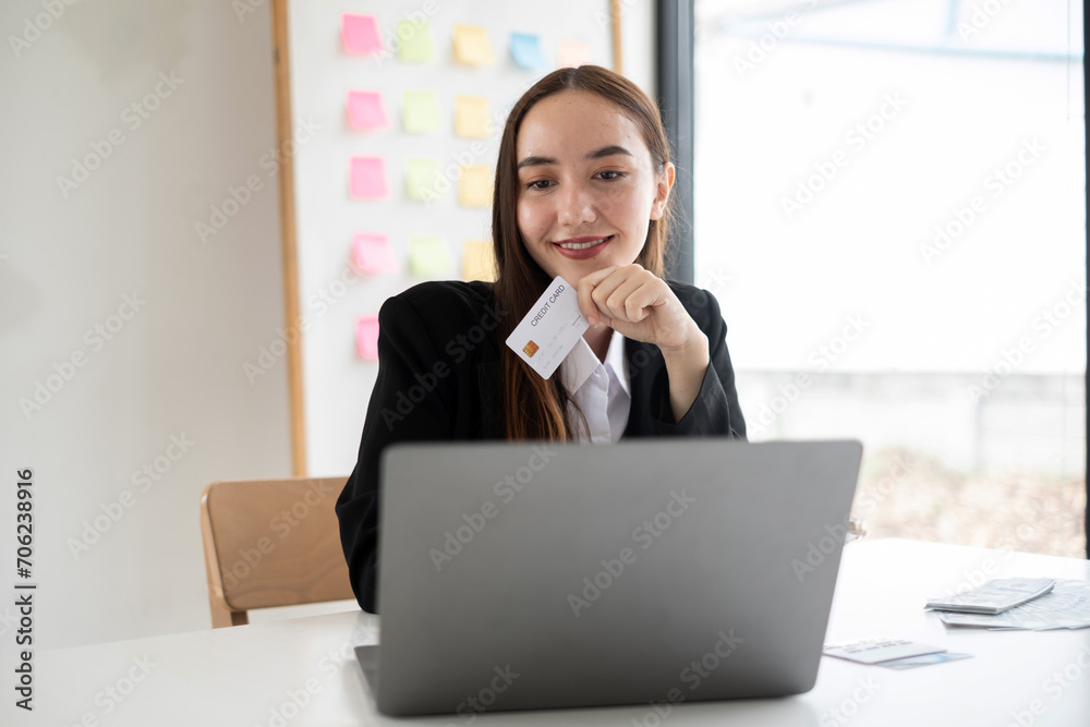 Asian girl shopping online holding credit and using laptop enter their card number in the mobile phone app to purchase and payment in internet store Asian girl shopping online holding credit and using laptop enter their card number in the mobile phone app to purchase and payment in internet store