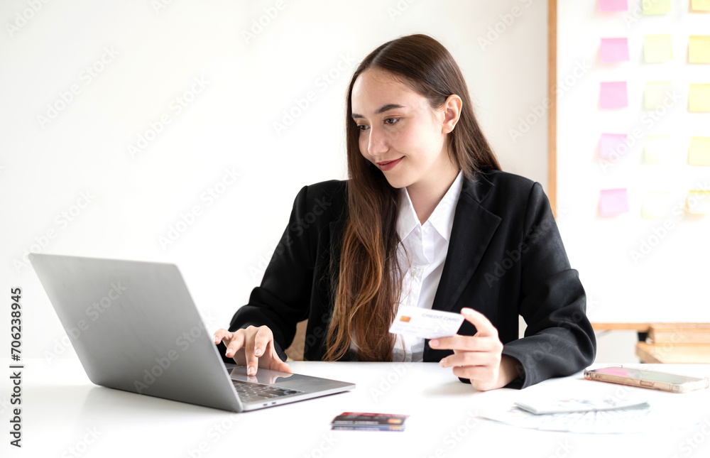 Asian girl shopping online holding credit and using laptop enter their card number in the mobile phone app to purchase and payment in internet store Asian girl shopping online holding credit and using laptop enter their card number in the mobile phone app to purchase and payment in internet store