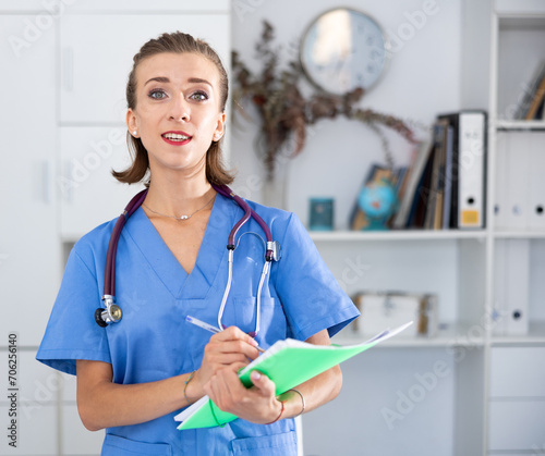 Cheefrul young woman therapist with stethoscope on shoulders holding paper folder. photo