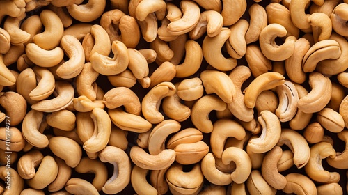 A large quantity of delicious raw cashews are arranged on a smooth tabletop in full frame top view.