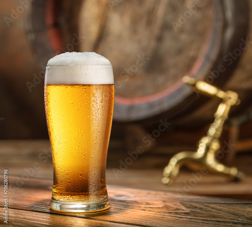 Glass of chilled beer and wooden beer cask on the background.