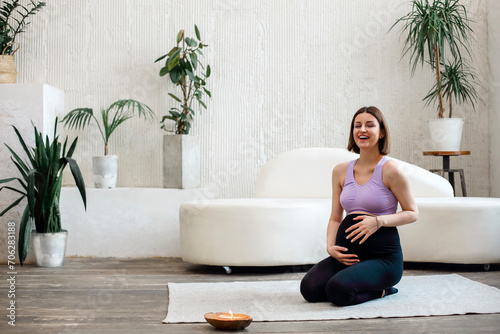 Beautiful pregnant woman sitting in yoga position in spa room, by coco candle