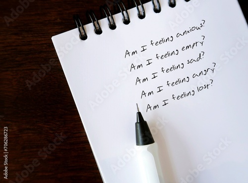 Pencil writing questions on notebook to to schedule a daily mental health check-in (Am I feeling anxious? empthy? sad? angry? lost?