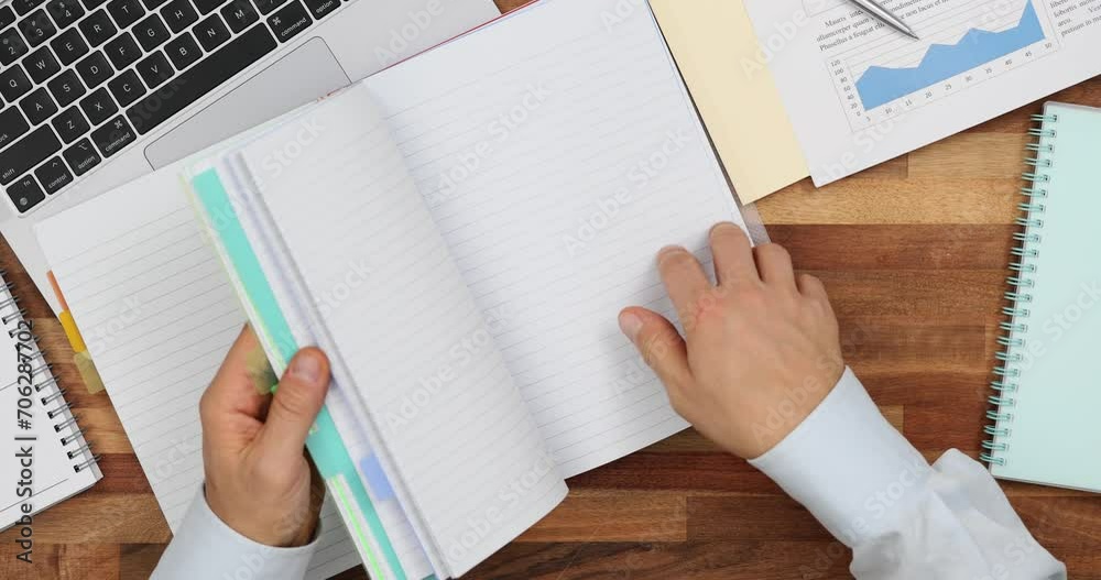 Man hand flips through blank colored notebook at workplace top view
