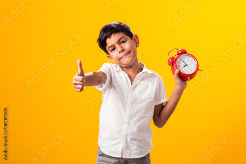 Kid boy holding alarm clock and showing thumb up gesture. Education and time management concept