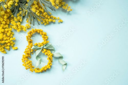International Women's Day. A banner, a flyer, a beautiful postcard for March 8th. Yellow mimosa flowers in the shape of the number eight and a ribbon bow on a turquoise, blue background. photo