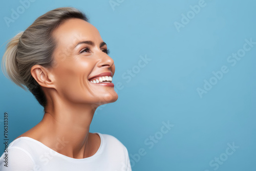 happy middle aged woman with beautiful smile on blue background, copy space