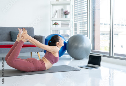 Beautiful smiling Female wearing sportswear exercise training yoga in living room. Attractive asian young fitness woman stretching body warming up before workout at home.