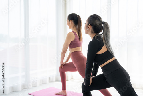 Teacher assists to do yoga pose training stretching body workout on mat at home for good health and body shape. Two asian fitness woman practicing yoga lesson course.