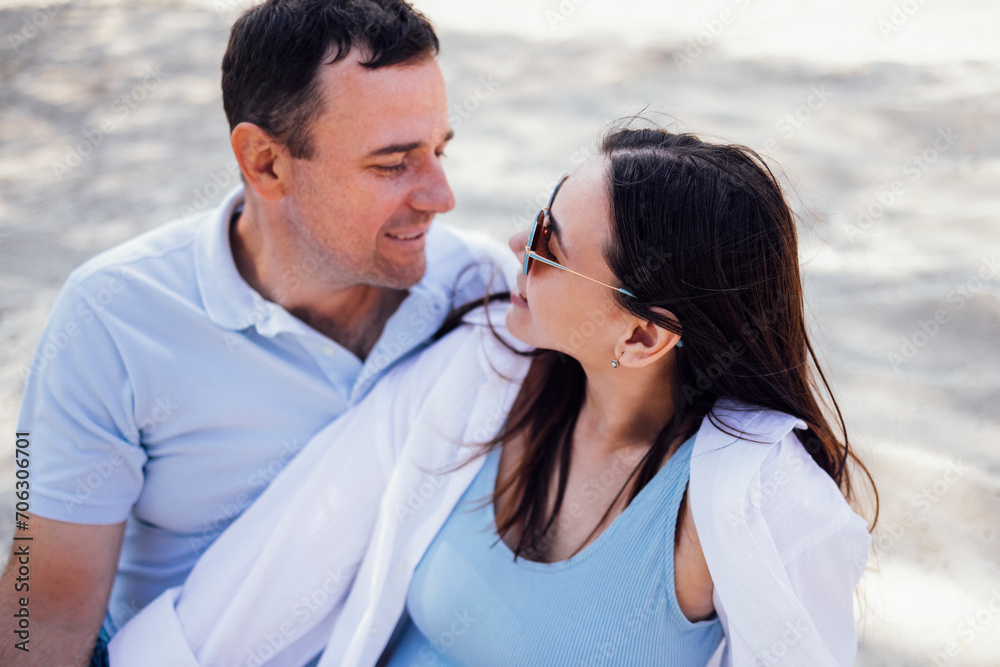 Caucasian couple in love on a sandy beach. Young man lovingly looks at a beautiful woman in sunglasses. Caucasian couple in love on a sandy beach. Young man lovingly looks at a beautiful woman in sunglasses.