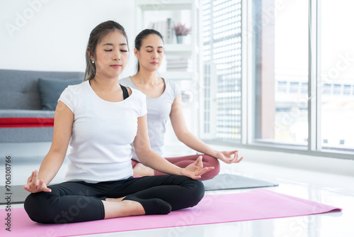 Two Young beautiful asian sport women sitting on the yoga mat practicing meditation. Fitness or exercise at home. Beautiful females relaxing after workout.