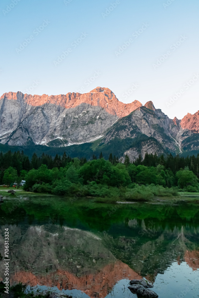 Morning sunrise view of Superior Fusine Lake (Laghi di Fusine) with majestic Mount Mangart in background in Tarvisio, Friuli Venezia Giulia, Italy. Captivating Water Reflection in tranquil atmosphere