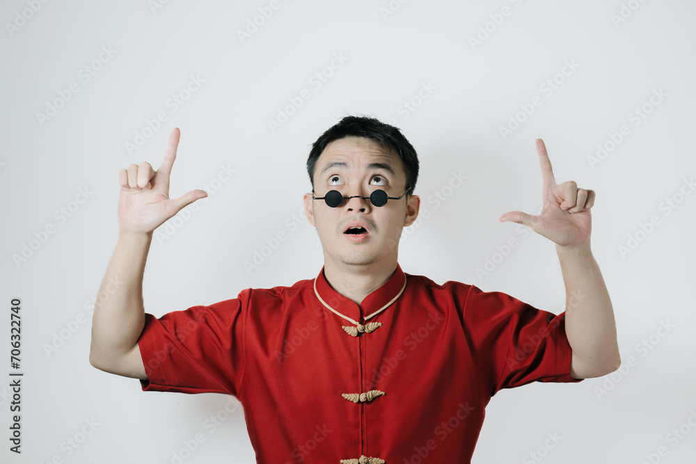 Asian man wearing traditional costume is pointing up on white background. Chinese New Year concept. Gong Xi Fa Cai. Asian man wearing traditional costume is pointing up on white background. Chinese New Year concept. Gong Xi Fa Cai.