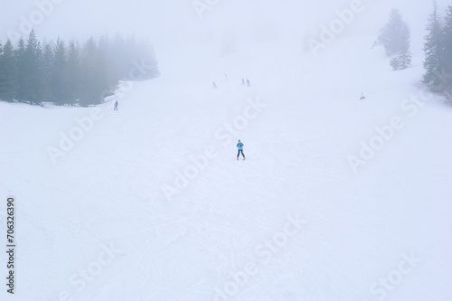 a slope at a ski resort, people skiing, snow pine trees, dense fog