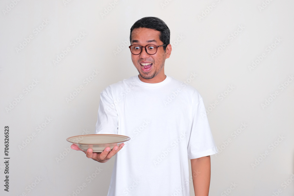 Asian man showing amazed expression when looking to empty dinning plate that he hold Asian man showing amazed expression when looking to empty dinning plate that he hold