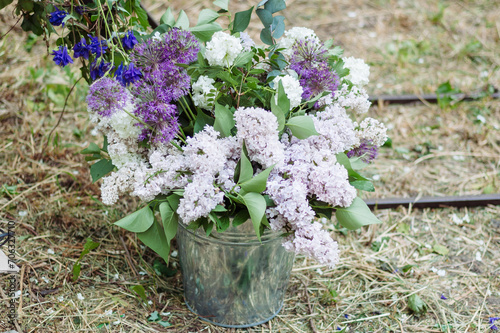 Fototapeta Naklejka Na Ścianę i Meble -  Celebratory Blooms: Lilac Peonies, Giant Onions, and Carnations in a Decorative Bucket, Elevating Outdoor Events and Weddings with Fresh Floral Elegance.